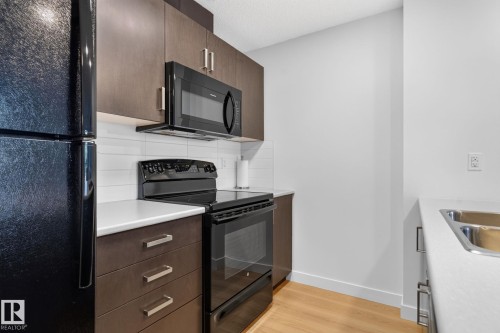 Modern kitchen featuring dark wood-finish cabinetry, white countertops, and a white subway tile backsplash - #203 5521 7 Av Sw, Edmonton, AB - Indoor Photo Showing Kitchen With Double Sink