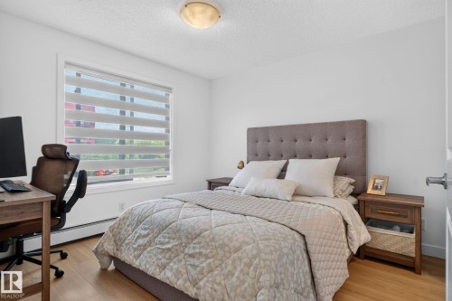 Bedroom featuring light wood-finish flooring, a contemporary ceiling light fixture, a window with horizontal blinds, and a neutral color palette - #203 5521 7 Av Sw, Edmonton, AB - Indoor Photo Showing Bedroom