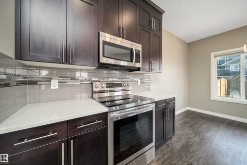 Kitchen featuring dark wood-finish cabinetry, stainless steel appliances, light-toned countertops, and a subway tile backsplash with decorative accents - 114 James Crescent, St. Albert, AB - Indoor Photo Showing Kitchen