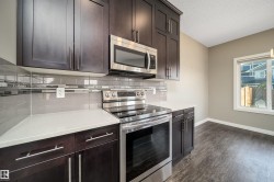 Kitchen featuring dark wood-finish cabinetry, stainless steel appliances, light-toned countertops, and a subway tile backsplash with decorative accents - 