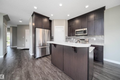 Kitchen featuring dark wood-finish cabinetry, stainless steel appliances, a center island with white countertop, and wood-finish flooring - 114 James Crescent, St. Albert, AB - Indoor Photo Showing Kitchen With Upgraded Kitchen