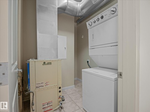 Dedicated laundry area featuring a white stacked washer and dryer unit, ceramic tile flooring, and exposed galvanized ductwork - #707 9819 104 St Nw, Edmonton, AB 