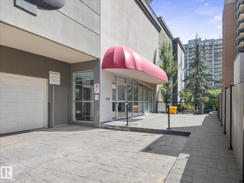 Building exterior featuring a red fabric awning, floor-to-ceiling glass storefront, and a concrete paver entrance - #707 9819 104 St Nw, Edmonton, AB 