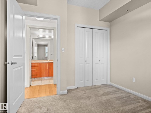 Carpeted room with neutral wall tones and white bi-fold closet doors - #707 9819 104 St Nw, Edmonton, AB 