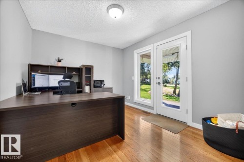 Light-filled room featuring wood-finish flooring, neutral wall tones, a modern ceiling light fixture, and a glass-paneled exterior door with an accompanying sidelight - #47 21061 Wye Rd, Rural Strathcona County, AB - Indoor Photo Showing Office