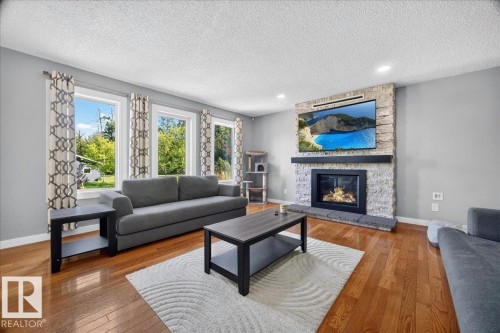Living area featuring hardwood flooring, a stacked stone fireplace with a dark mantel, and recessed lighting - #47 21061 Wye Rd, Rural Strathcona County, AB - Indoor Photo Showing Living Room With Fireplace