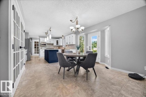 Spacious dining area featuring neutral tile flooring, a large bay window, and a glass-paneled door opening to the exterior - #47 21061 Wye Rd, Rural Strathcona County, AB - Indoor Photo Showing Dining Room