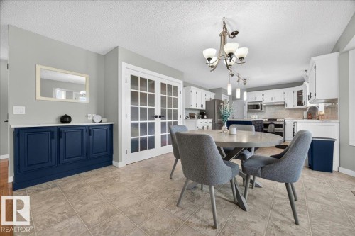 Spacious kitchen and dining area featuring a chandelier, tile flooring, white shaker cabinetry, stainless steel appliances, and a built-in blue cabinet - #47 21061 Wye Rd, Rural Strathcona County, AB - Indoor Photo Showing Dining Room