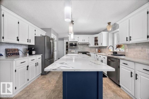 Kitchen featuring a central island with a blue base and a white veined countertop, complemented by white cabinetry with dark hardware - #47 21061 Wye Rd, Rural Strathcona County, AB - Indoor Photo Showing Kitchen