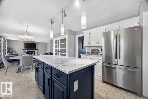 Kitchen island featuring a white-veined countertop, dark blue cabinetry, and track lighting with pendant fixtures - #47 21061 Wye Rd, Rural Strathcona County, AB - Indoor Photo Showing Kitchen With Upgraded Kitchen