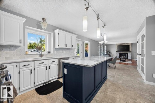 Open-concept kitchen featuring a large central island with a white stone countertop, white cabinetry with dark hardware, stainless steel appliances, and a tiled backsplash - #47 21061 Wye Rd, Rural Strathcona County, AB - Indoor Photo Showing Kitchen With Upgraded Kitchen