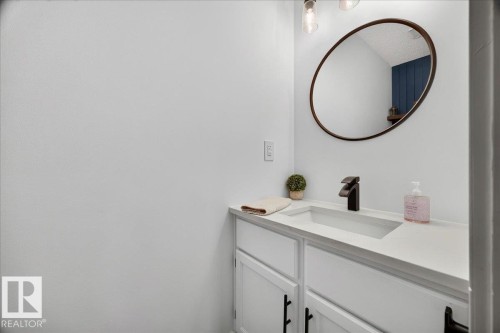 White vanity with an integrated rectangular sink, matte black faucet, and a large oval mirror - #47 21061 Wye Rd, Rural Strathcona County, AB - Indoor Photo Showing Bathroom