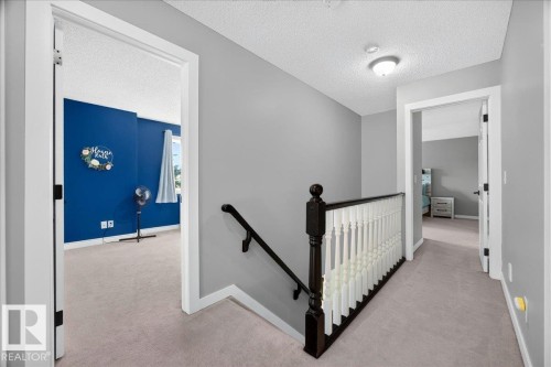 Upper-level hallway with light gray walls, plush carpeting, and a dark wood newel post and handrail with white balusters - #47 21061 Wye Rd, Rural Strathcona County, AB - Indoor Photo Showing Other Room