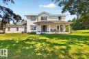 Two-story residence featuring light-colored siding with dark trim accents, a covered front porch, an expansive front lawn, and mature trees - #47 21061 Wye Rd, Rural Strathcona County, AB  - Outdoor With Deck Patio Veranda 