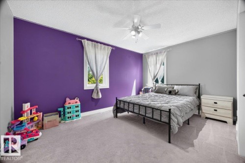Bedroom featuring a purple accent wall, two windows, and light gray carpeting - #47 21061 Wye Rd, Rural Strathcona County, AB - Indoor Photo Showing Bedroom