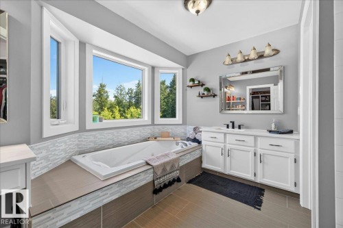 Soaking tub with a tiled surround, bay windows, white cabinetry with dark hardware, quartz countertop, and large format floor tiles - #47 21061 Wye Rd, Rural Strathcona County, AB - Indoor Photo Showing Bathroom