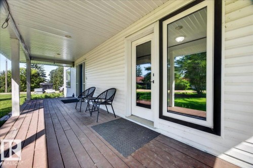 Covered front porch featuring wood-finish decking, white vinyl siding, and white soffit - #47 21061 Wye Rd, Rural Strathcona County, AB - Outdoor With Deck Patio Veranda With Exterior