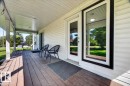 Covered front porch featuring wood-finish decking, white vinyl siding, and white soffit - #47 21061 Wye Rd, Rural Strathcona County, AB  - Outdoor With Deck Patio Veranda With Exterior 