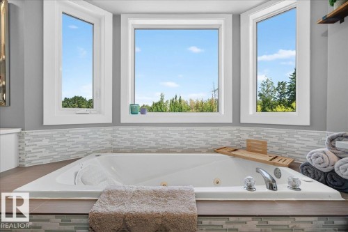 Built-in jetted tub surrounded by a decorative tile backsplash and wood-finish ledge - #47 21061 Wye Rd, Rural Strathcona County, AB - Indoor Photo Showing Bathroom