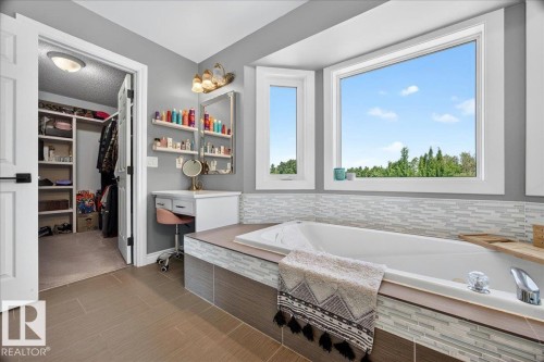 Built-in soaking tub with a tiled surround, large bay window, integrated vanity area, and wood-finish flooring - #47 21061 Wye Rd, Rural Strathcona County, AB - Indoor Photo Showing Bathroom