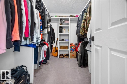Walk-in closet featuring carpet flooring, built-in shelving, and white paneled doors with dark hardware - #47 21061 Wye Rd, Rural Strathcona County, AB - Indoor With Storage