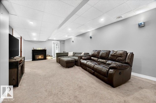 Spacious room featuring carpeting, a built-in fireplace with a dark mantel, light gray walls, white baseboards, and a white acoustic tile ceiling with recessed lighting - #47 21061 Wye Rd, Rural Strathcona County, AB - Indoor With Fireplace