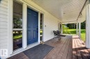 Covered front porch featuring wood-finish flooring, white siding, and an opaque blue entry door with clear side panels - #47 21061 Wye Rd, Rural Strathcona County, AB  - Outdoor With Deck Patio Veranda With Exterior 
