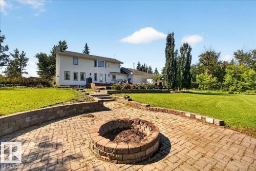 Expansive backyard featuring a brick paver patio with a built-in fire pit, terraced landscaping with retaining walls, and a large manicured lawn - #47 21061 Wye Rd, Rural Strathcona County, AB - Outdoor With Deck Patio Veranda