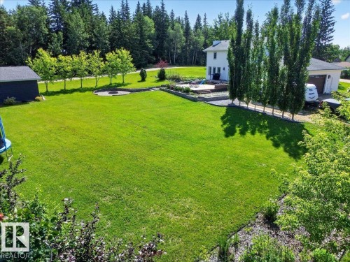 Expansive rear yard featuring a manicured lawn, established trees, and a fire pit area with stone surround - #47 21061 Wye Rd, Rural Strathcona County, AB - Outdoor