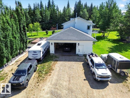 Detached residence featuring a two-car garage with a gravel driveway, surrounded by mature trees and a manicured lawn - #47 21061 Wye Rd, Rural Strathcona County, AB - Outdoor