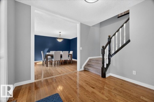 Entryway featuring wood-finish flooring, a carpeted staircase with white balusters and dark wood newel posts, and a wide cased opening to a dining area - #47 21061 Wye Rd, Rural Strathcona County, AB - Indoor Photo Showing Other Room