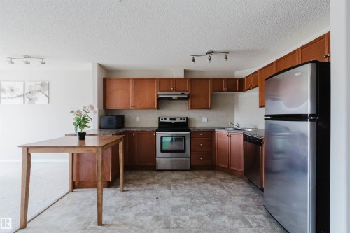 Modern kitchen featuring wood-finish cabinetry, stainless steel appliances, and a built-in dishwasher - #7306 7327 South Terwillegar Dr Nw, Edmonton, AB - Indoor Photo Showing Kitchen With Double Sink