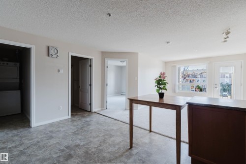 Spacious interior featuring a combination of resilient flooring and carpeting, a laundry closet with stacked appliances, and a living area with a large window and balcony door - #7306 7327 South Terwillegar Dr Nw, Edmonton, AB - Indoor