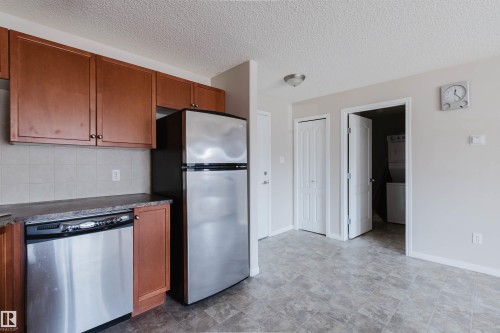Kitchen area featuring wood-finish cabinetry, stainless steel dishwasher, stainless steel refrigerator, and tiled backsplash - #7306 7327 South Terwillegar Dr Nw, Edmonton, AB - Indoor Photo Showing Kitchen
