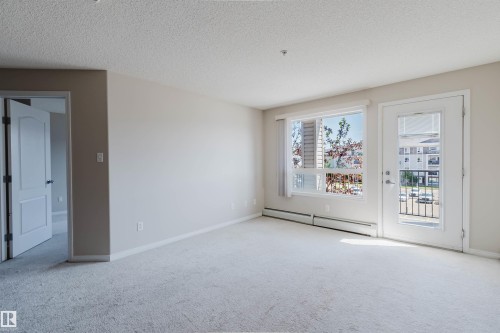 Spacious room featuring light-toned carpet flooring, a large window, and a glass-paneled door opening to a balcony with metal railings - #7306 7327 South Terwillegar Dr Nw, Edmonton, AB - Indoor Photo Showing Other Room