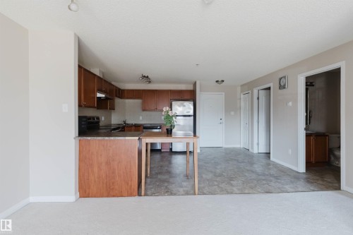 Open-concept living area featuring a kitchen with wood cabinetry, stainless steel appliances, and a breakfast bar - #7306 7327 South Terwillegar Dr Nw, Edmonton, AB - Indoor Photo Showing Kitchen