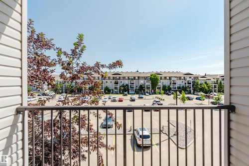 Balcony featuring horizontal siding, a metal railing, and a partial view of a paved parking area and distant multi-story residential buildings - #7306 7327 South Terwillegar Dr Nw, Edmonton, AB - Outdoor With Balcony