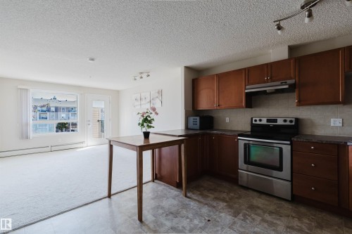 Kitchen area featuring wood-finish cabinetry, stainless steel range, and stone-look countertops - #7306 7327 South Terwillegar Dr Nw, Edmonton, AB - Indoor Photo Showing Kitchen