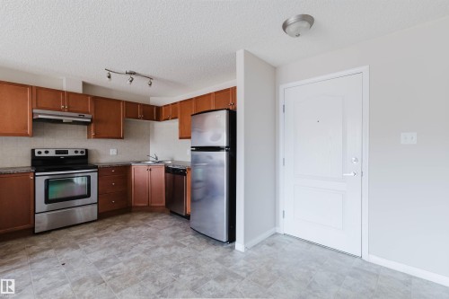 Kitchen featuring wood cabinetry, stainless steel appliances, track lighting, and a neutral tile backsplash - #7306 7327 South Terwillegar Dr Nw, Edmonton, AB - Indoor Photo Showing Kitchen