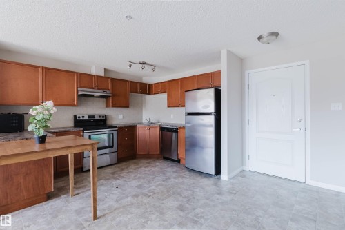 Open-concept kitchen featuring wood cabinetry, stainless steel appliances, and laminate countertops - #7306 7327 South Terwillegar Dr Nw, Edmonton, AB - Indoor Photo Showing Kitchen