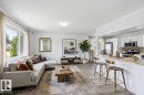 Open-concept living area featuring a kitchen island with seating, wood-finish flooring, white cabinetry, and stainless steel appliances - 13524 62 Street Nw, Edmonton, AB  - Indoor 