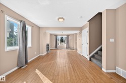 Open-concept living area featuring wood-finish flooring, neutral wall tones, multiple windows, a modern fireplace, and a carpeted staircase - 