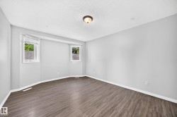 Spacious room featuring wood-finish flooring, light grey painted walls, white baseboards, and a textured white ceiling - 
