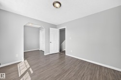 Spacious room featuring wood-finish flooring, light grey walls, white baseboards, a white paneled door, and a flush mount ceiling light - 
