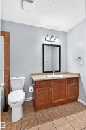 Bathroom featuring a wood-finish vanity with a light-colored countertop, an undermount sink, and a framed mirror with a three-light fixture - 