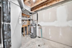 Unfinished basement utility area featuring a water heater, visible ductwork, and exposed ceiling joists - 