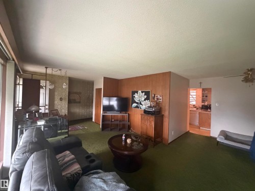 Carpeted living area featuring wood-paneled walls and a ceiling fan - 13207 117 Street, Edmonton, AB 
