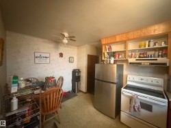 Kitchen area featuring a stainless steel refrigerator, white electric range with overhead ventilation, wood-finish cabinetry, and patterned vinyl flooring - 