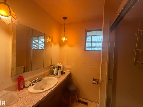 Bathroom featuring a built-in vanity with an integrated sink, a large wall-mounted mirror, and a window providing natural light - 13207 117 Street, Edmonton, AB 