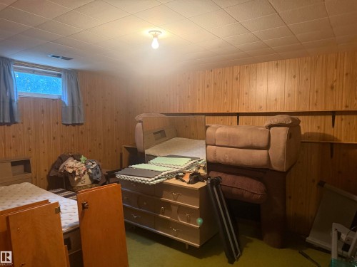 Lower-level room featuring wood paneling, a drop ceiling, and recessed windows - 13207 117 Street, Edmonton, AB 